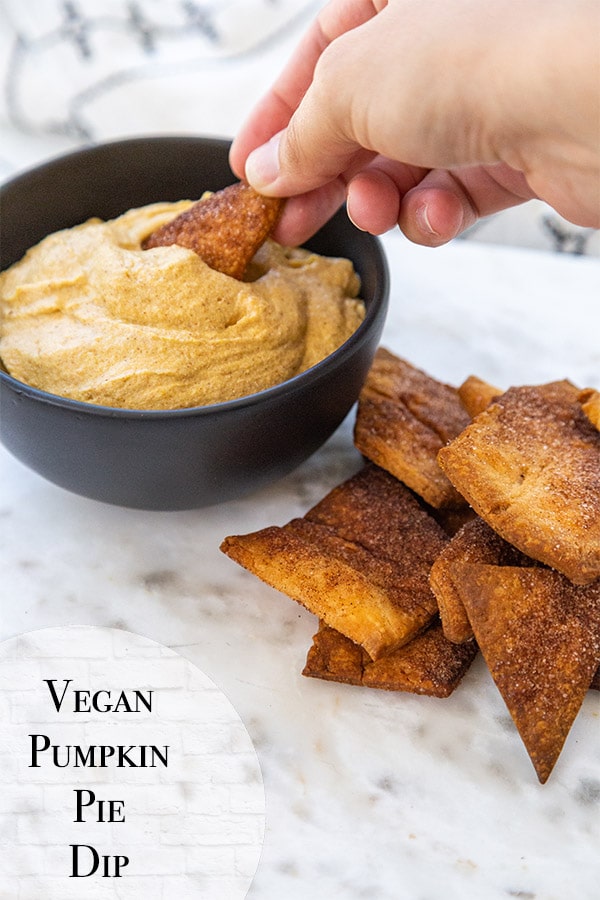 A Pinterest pin for vegan pumpkin dip with a hand dipping a pie crisp into a bowl of the dip. 