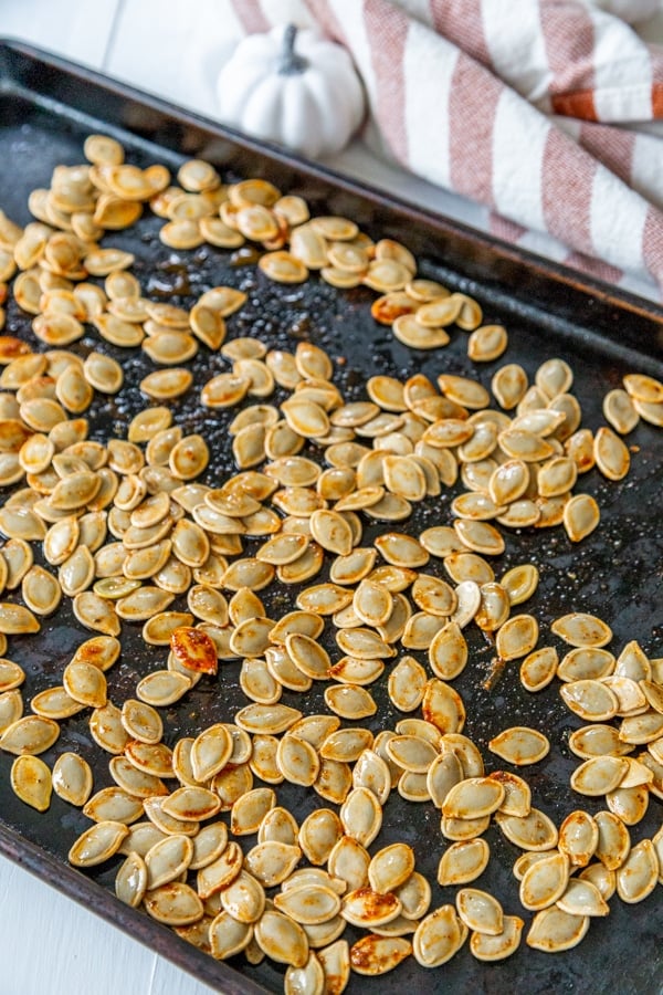Pumpkin seeds spread out on a rimmed baking sheet.