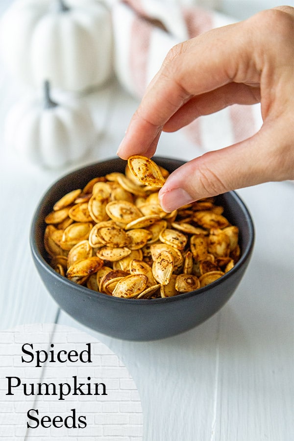 A PInterest pin for roasted pumpkin seeds with a picture of a hand taking the seeds out of a black bowl. 