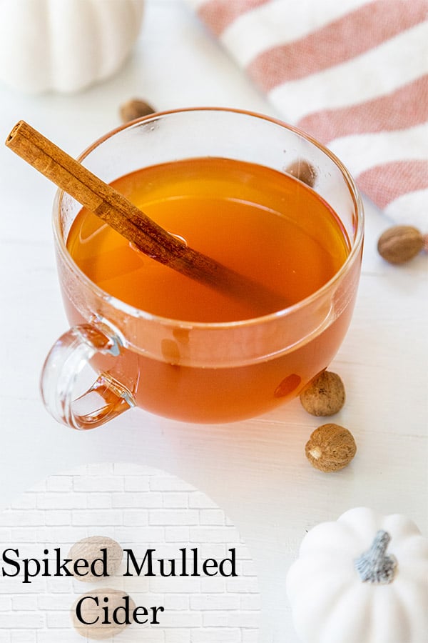 mulled spiked cider in a glass mug with a cinnamon stick, pumpkins, nutmeg, and an orange and white striped towel