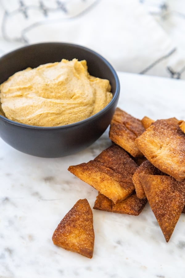 A black bowl with pumpkin dip and pie crust crisps. 