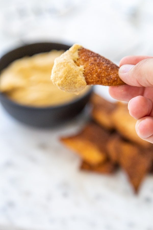 A hand holding a pie crust chip dipped into pumpkin dip. 