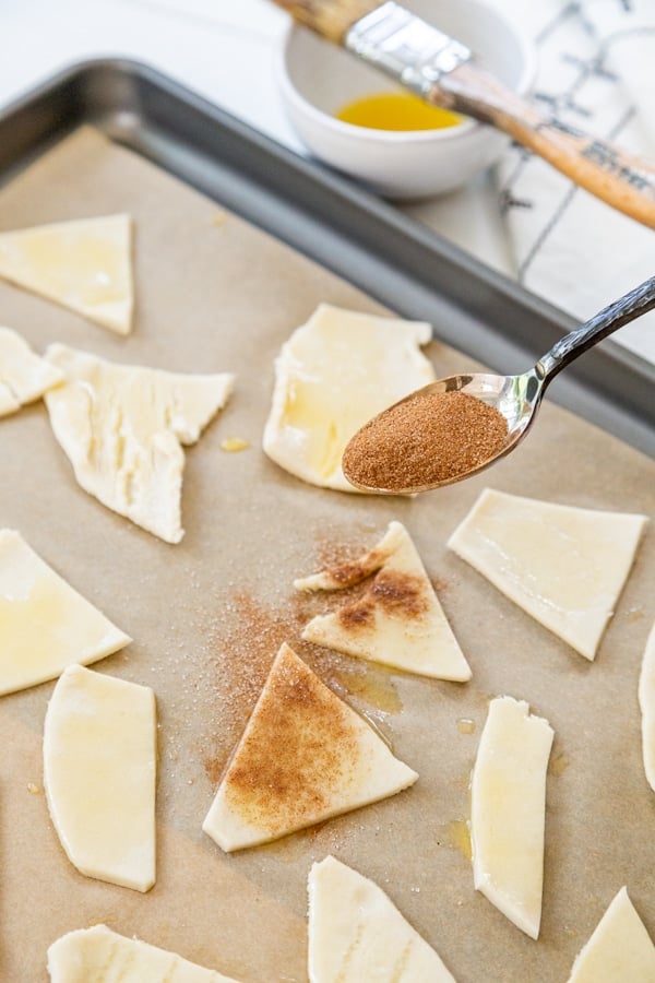 A hand sprinkling cinnamon sugar on pie crust chips.