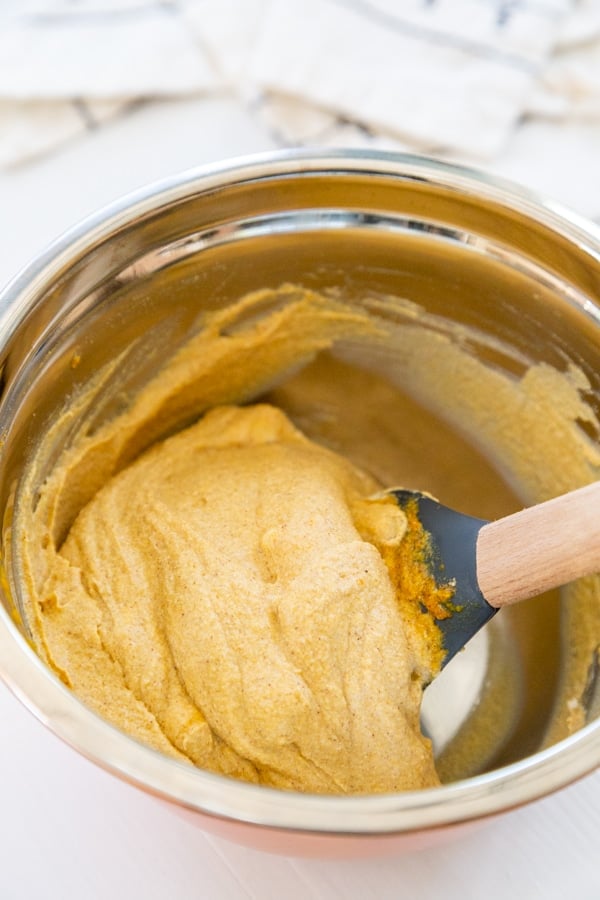 Ingredients for pumpkin dip being combined with a spatula in a mixing bowl.