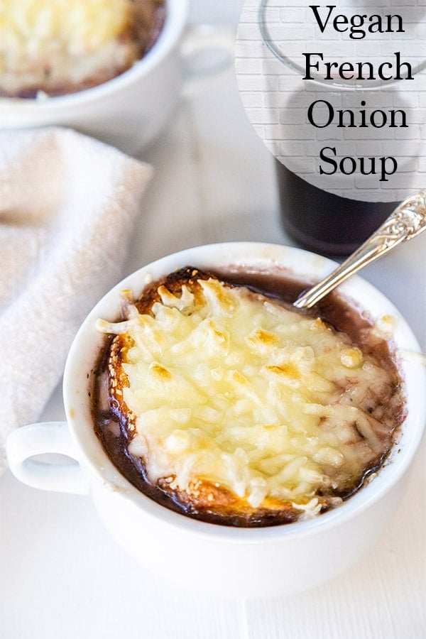 Vegan french onion soup with stretchy vegan cheese, baguette, and a red wine onion broth in a white soup bowl served with a glass of red wine