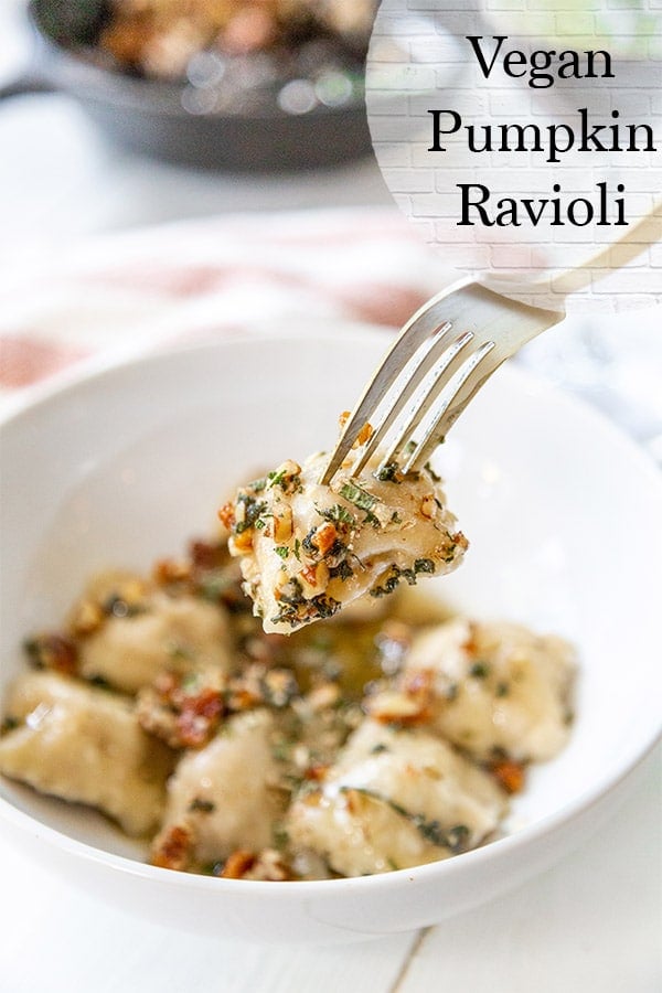 pumpkin ravioli being picked up by a fork topped with brown butter sage pecan sauce with an orange and white towel behind the bowl