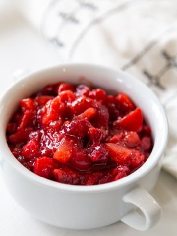 A white bowl with cranberry apple sauce next to a black and white napkin.