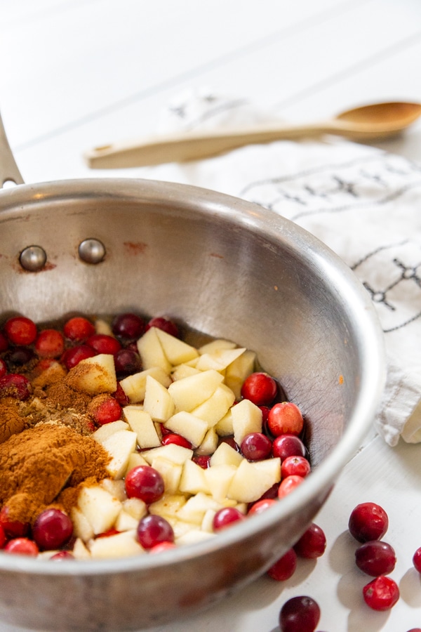 A copper bowl with cranberries, apples, brown sugar, and spices.