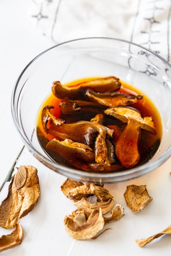 A clear glass bowl of dried porcini mushrooms in water.