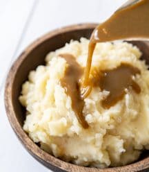 Gravy being poured over a bowl of mashed potatoes.