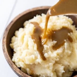 Gravy being poured over a bowl of mashed potatoes.