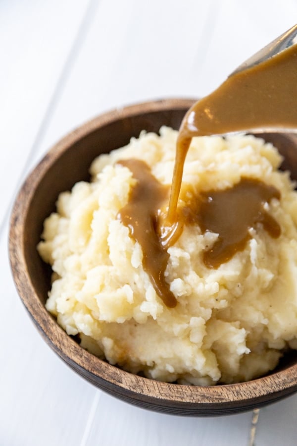 Gravy being poured over a bowl of mashed potatoes. 