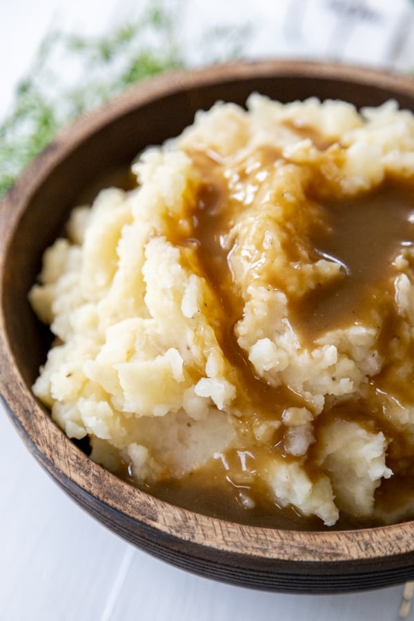 A wood bowl filled with mashed potatoes and brown gravy. 