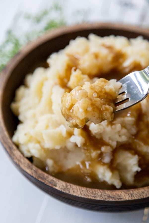 A fork taking a bite of mashed potatoes and gravy out of a wood bowl. 