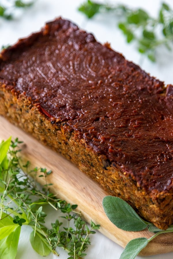 A lentil loaf on a wood board with fresh herbs next to it.