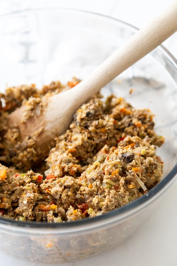 A clear glass bowl with a lentil loaf mixture being stirred with a wooden spoon.