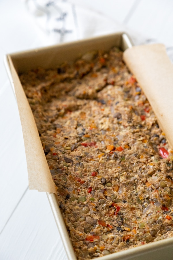An unbaked lentil loaf in a bread pan with parchment paper.