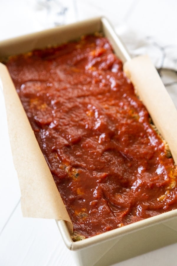 An unbaked lentil loaf in a bread pan with BBQ sauce spread on top.