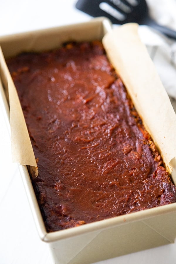 A lentil loaf in a bread pan with parchment paper on the sides of the pan.