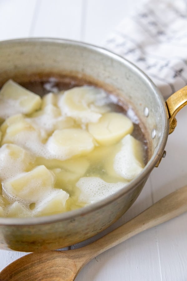 A copper pot filled with cubed potatoes and water.