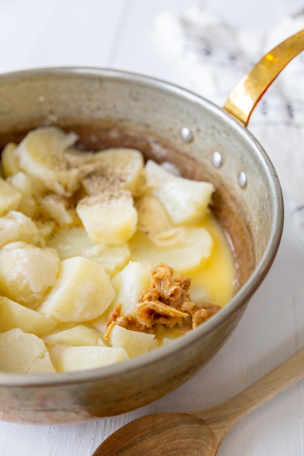 A copper pot with cooked potatoes and roasted garlic.