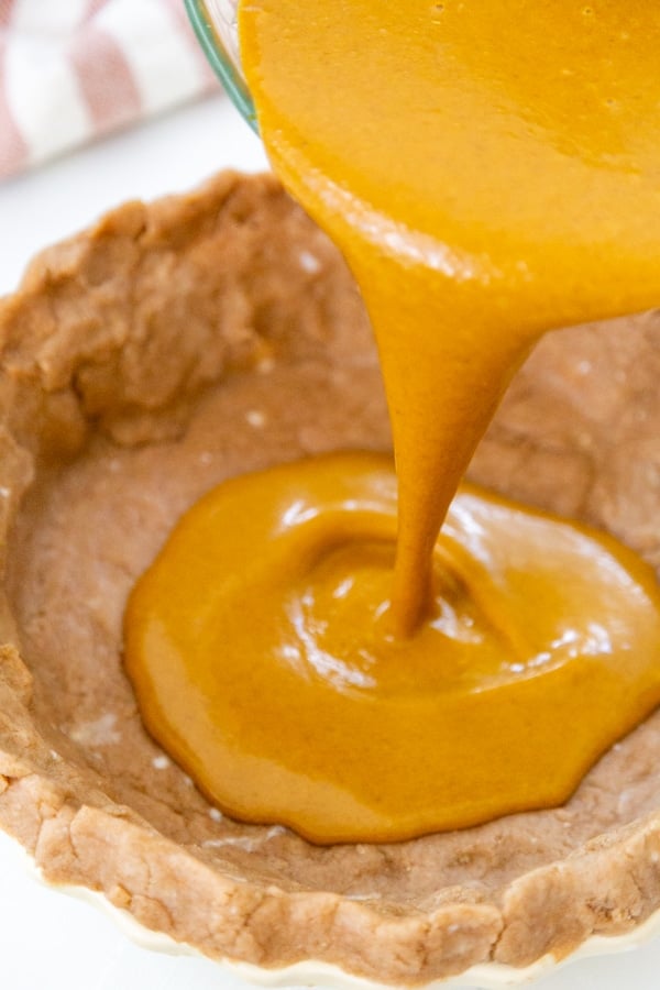 Pumpkin pie filling being poured into a pie crust.