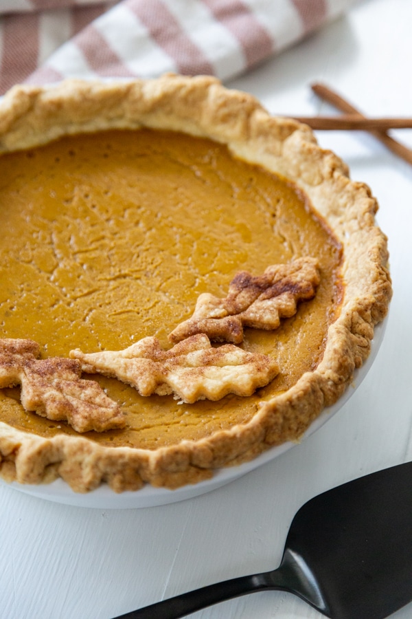 A pumpkin pie with pie crust leaves on top and a black pie spatula. 