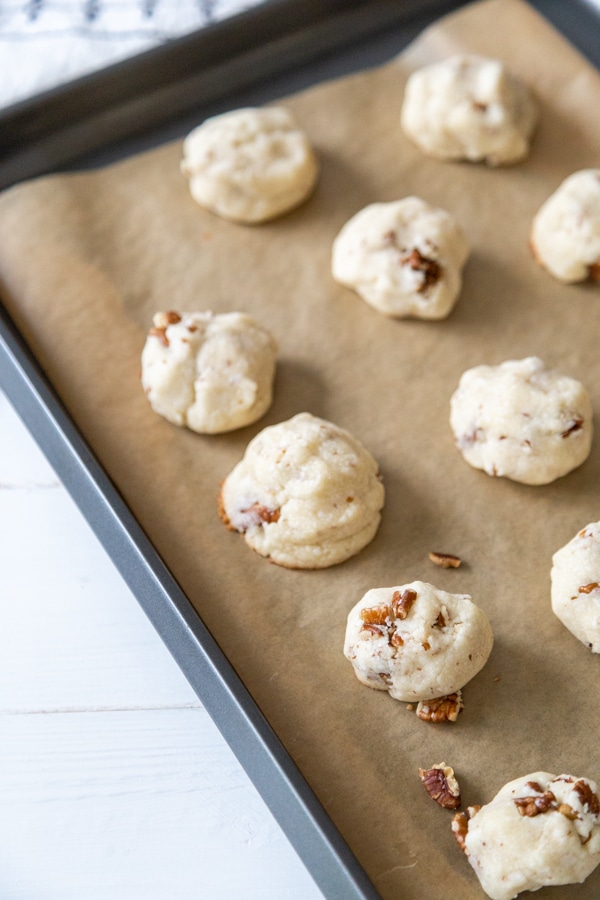 A cookie sheet with parchment paper and unbaked Russian Tea Cake cookies.