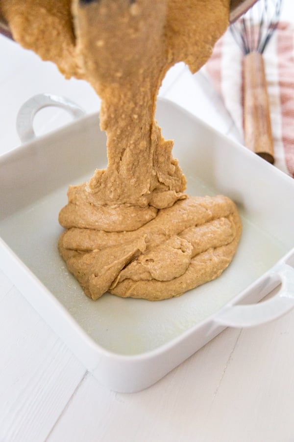 Spice cake batter being poured into a square white cake pan.