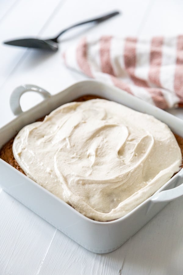 A square white ceramic pan with cake frosted with cream cheese frosting.