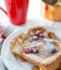A white plate with French toast and cranberry syrup and a red mug of coffee.