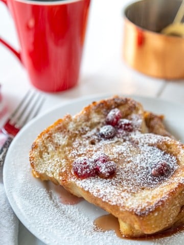 A white plate with French toast and cranberry syrup and a red mug of coffee.