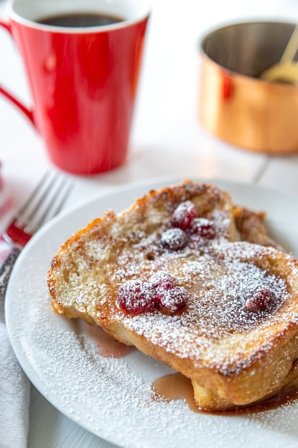 A white plate with French toast and cranberry syrup and a red mug of coffee.