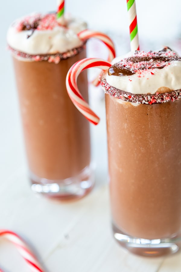 2 glasses of frozen hot chocolate with candy canes, whipped cream, and melted chocolate. 
