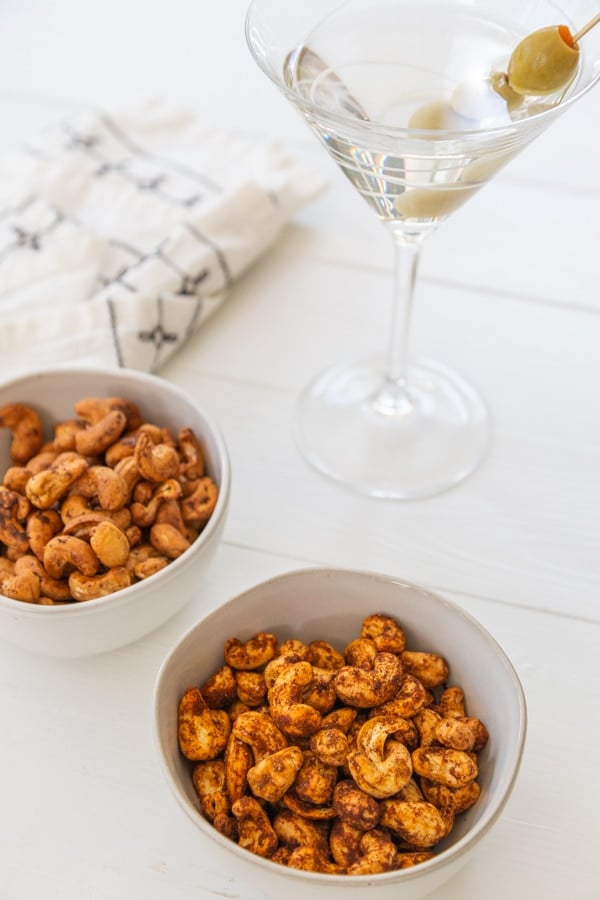 Two white bowls of spiced roasted nuts and a glass of martini.