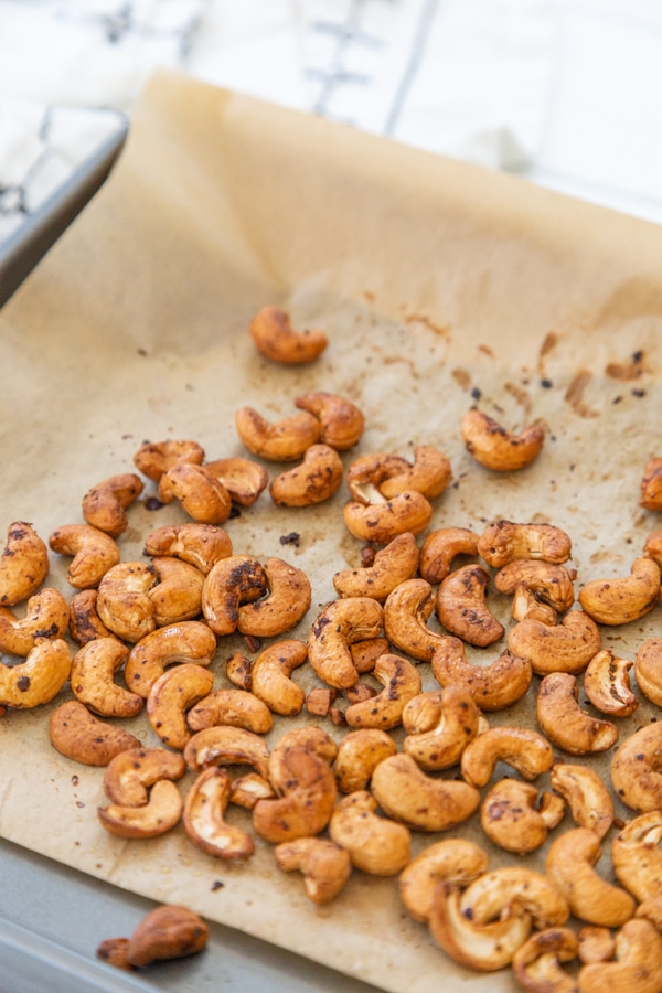 Roasted cashews on a parchment lined baking sheet.