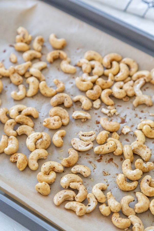 Raw cashews with liquid smoke on a parchment lined baking sheet.