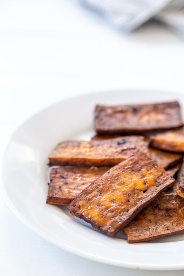 A stack of vegan tofu bacon on a white plate.