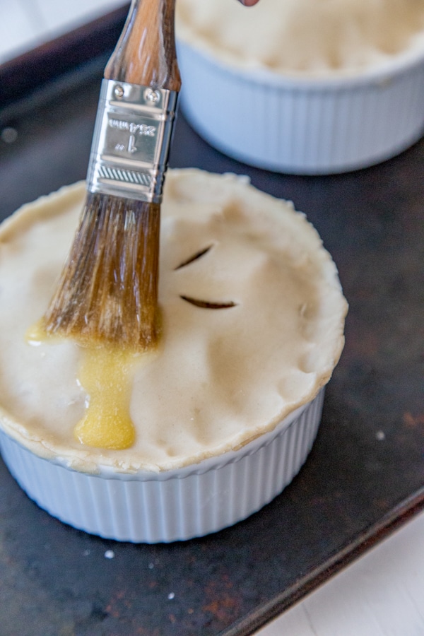 A pastry brush brushing melted butter on an uncooked pot pie.