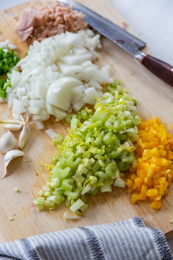 Chopped celery, onion, and bell pepper on a wood cutting board.