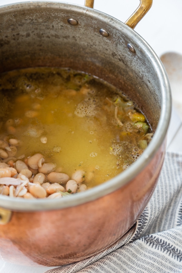 A copper pot with sauteed veggies, white beans, and broth.
