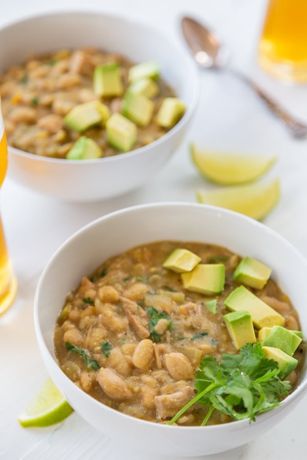 2 white bowls with white bean chili and cilantro and avocado on top. 