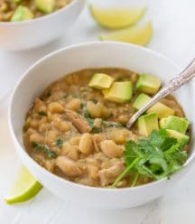 A bowl of white bean chili with avocado and cilantro on top and a spoon in the bowl.