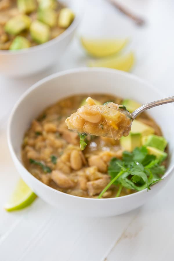 A spoon full of white bean chili over a white bowl of the chili. 