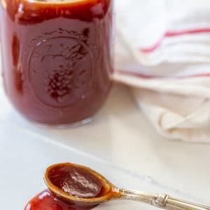 A mason jar with bbq sauce and a spoon with the sauce spilling over the side.