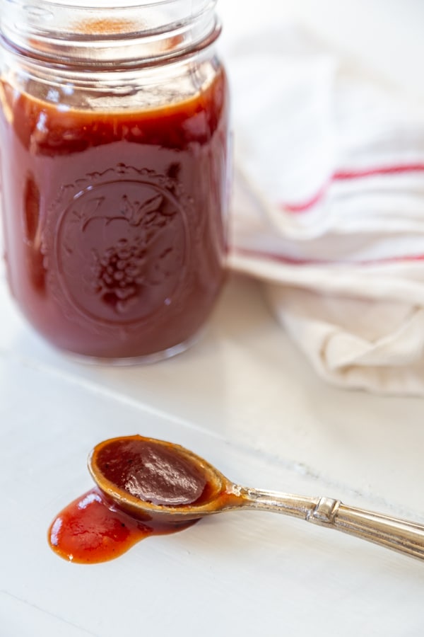 A mason jar with bbq sauce and a spoon with the sauce spilling over the side.