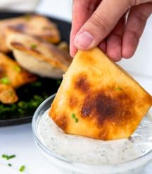 A hand dipping a calzone into a glass bowl of ranch dressing.