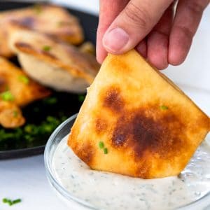 A hand dipping a calzone into a glass bowl of ranch dressing.