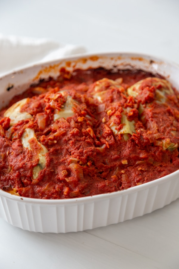 A white baking dish with stuffed cabbage covered in tomato sauce. 