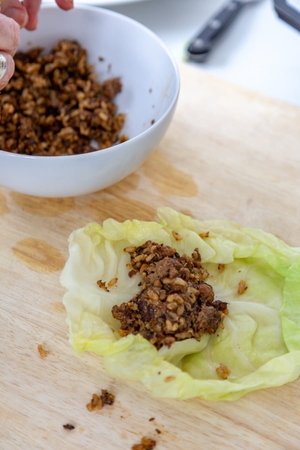 Meat filling in the middle of a cabbage leaf and a white bowl of filling next to it.